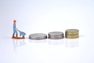 Beyaz arkaplanda bozuk para yığını olan çalışan bir minyatürün seçici odak görüntüsü. Yaşam konsepti