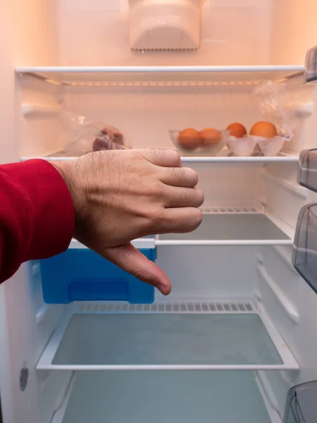 Photograph of a hand pointing down with an empty fridge in the background