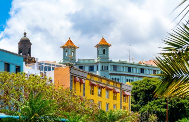 Palmiye ağaçları, renkli cepheleri ve Las Palmas 'ta bulutlu gökyüzünün altındaki Teatro Guiniguada kuleleri olan şehir manzarası