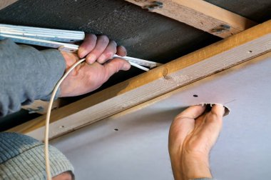 İşçi, kablo katlama kuralını ahşap alt yapıdan yuvarlak açılışa doğru yönlendiriyor, iç inşaatta elektrik tesisatı için hazırlık çalışması, görünür ahşap altyapı