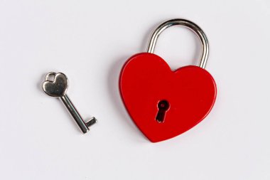 Kilit şeklinde metalik kırmızı bir kalp ve beyaz arkaplanda metal bir anahtar.