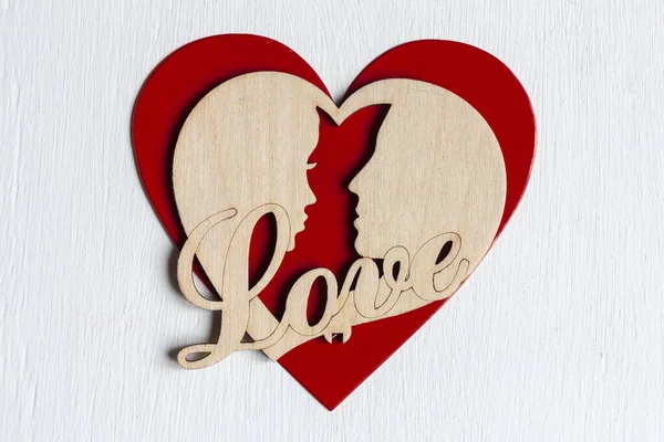 a wooden heart with two lovers and a Love lettering on a red heart on white background