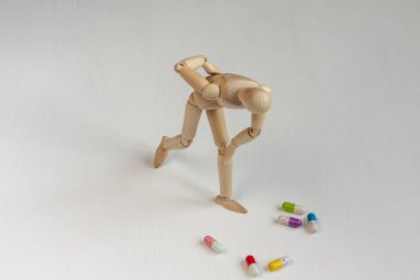 Beyaz arka planda renkli hapların arasında sırt ağrısı olan eğri büğrü tahta bir manken.