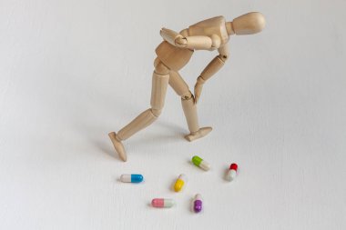 Beyaz arka planda renkli hapların arasında sırt ağrısı olan eğri büğrü tahta bir manken.