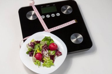 Beyaz tabakta biraz salata ve beyaz arkaplanda siyah pulların üzerinde duran pembe bir santimetre.