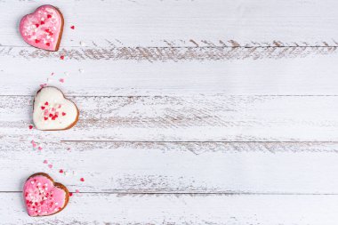 Beyaz ahşap arka planda küçük kalplerle çevrili pembe kalp şeklinde zencefilli ekmek.
