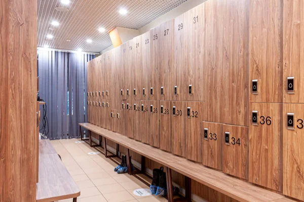 light brown lockers with numbers and a bench in a locker room