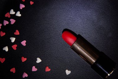 Küçük beyaz, pembe ve kırmızı kalpler ve siyah arkaplanda kırmızı ruj.