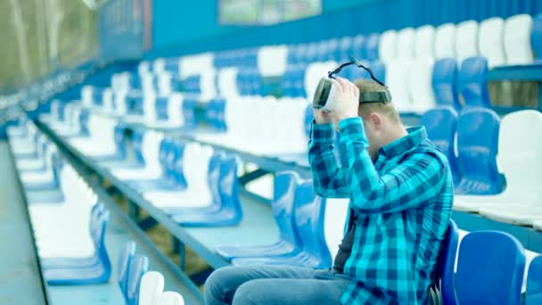 Man sitting on the tribune and putting on VR glasses — Stock Video