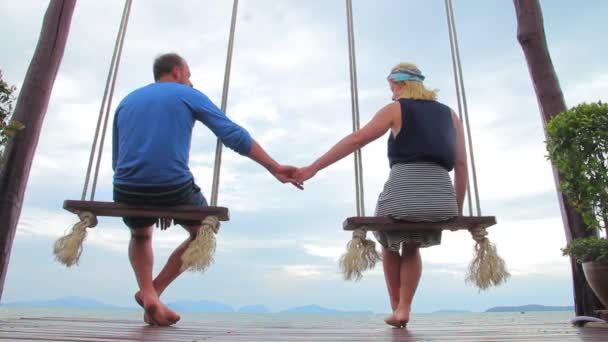 Молода пара сидить на гойдалці, милуючись природою — стокове відео