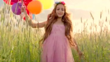 Young girl running through a wheat field with colour balloons during sunset