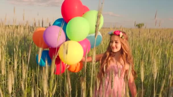 Giovane ragazza che gira nel campo di grano con palloncini di colore durante il tramonto — Video Stock