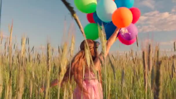Молодая девушка крутится на пшеничном поле с цветными шариками на закате — стоковое видео