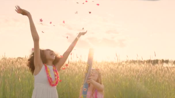 Young girls exploding party cracker in the wheat field and merrily catching the falling confetti during sunset — Stock video