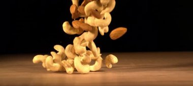 Badem ve kaju fıstıklarının süper yavaş çekimi ahşap masaya düşer. Sağlıklı atıştırmalıklar, tatmin edici çıtırtılar. Siyah arka plan