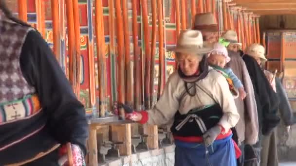 Pilgrims walk past prayer wheels in Xiahe. — Stock Video