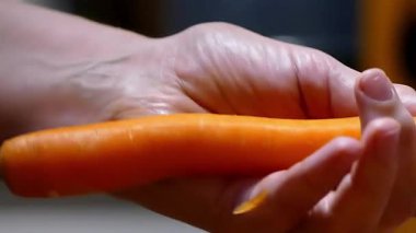 Temiz beyaz arka planda metal kabuklu taze, canlı turuncu bir havucu soyan ellerin yakın çekimi. Sağlıklı beslenme, yemek pişirme ve yemek hazırlama kavramı.