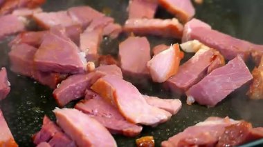 Küçük çiğ et parçaları fırının üstünde siyah bir tavada pişiriliyor.