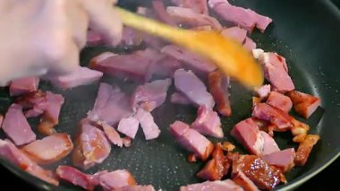 Küçük çiğ et parçaları fırının üstünde siyah bir tavada pişiriliyor.