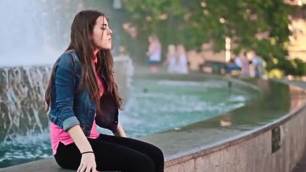 Дівчина сидить біля фонтану — стокове відео