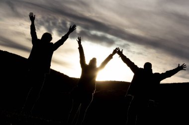 Bulutlu gökyüzünde elleri havada üç kişinin siyah siluetleri. Arka ışık. Boşluğu kopyala.