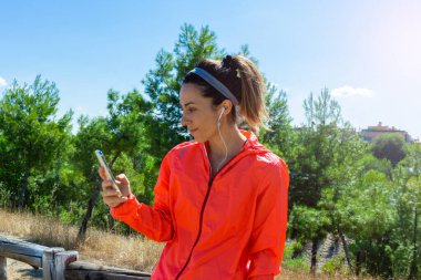 Koştuktan sonra akıllı telefondan sonuçlarına bakarken dinlenen genç bir kadın. Sağlıklı bir yaşam tarzı. Seçici odak.