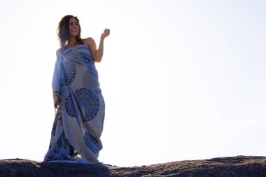 Bikinili genç bir kız bir kayanın tepesinde rüzgarla hareket eden bir havlu tutuyor. Uzayı kopyala Seçici odak.