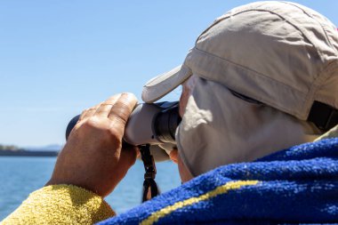 Olgun bir adam gölde dürbünle sonsuzluğa bakıyor. Seçici odak.