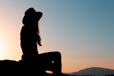 Sonbaharda günbatımında şapkasıyla oturan kadın silueti. Uzayı kopyala Seçici odak.