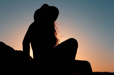 Sonbaharda günbatımında şapkasıyla oturan kadın silueti. Uzayı kopyala Seçici odak.