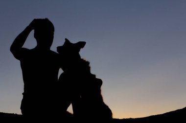 Gün batımında köpeğiyle oynayan bir adamın silueti. Arka ışık. Boşluğu kopyala.