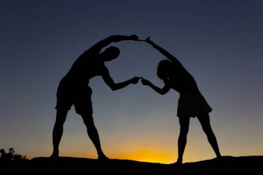 Genç çift gün batımında vücutlarıyla ışığa karşı figürler yapıyor. Boşluğu kopyala.