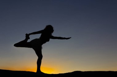 Gün batımında doğada bir kayanın üzerinde yoga yapan bir kadın silueti. Arka ışık. Boşluğu kopyala.