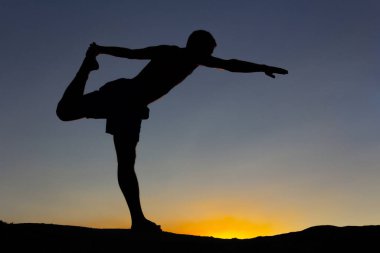 Gün batımında doğada bir kayanın üzerinde yoga yapan bir adamın silueti. Arka ışık. Boşluğu kopyala.