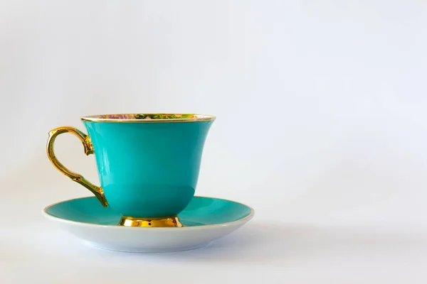 Cyan tea or coffee cup with gold trim on white background. Selective focus. Copy space.