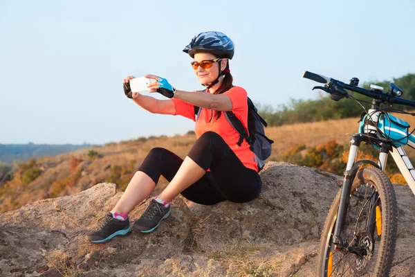 Adult attractive female cyclist sits on the rock and makes the p — Stock Photo, Image