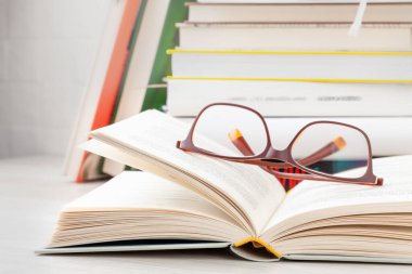Okuma gözlüğü, açık bir kitap ve arka plan olarak bir yığın kitap..