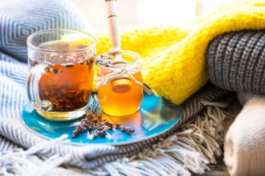 Fincan çay ve kavanoz mavi tabakta bal, arka planda örme giyim