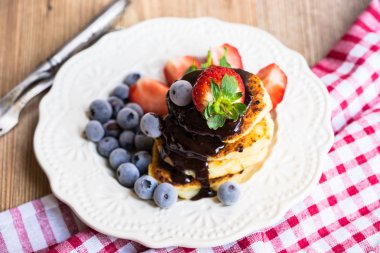 Eritilmiş çikolata, çilek ve beyaz bir plaka üzerinde yaban mersini ile Pancakes