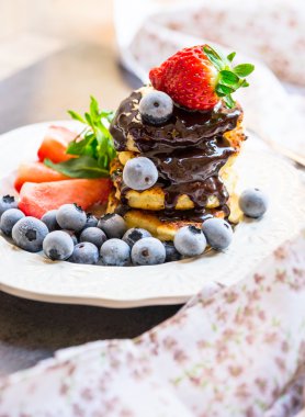 Eritilmiş çikolata, çilek ve beyaz bir plaka üzerinde yaban mersini ile Pancakes