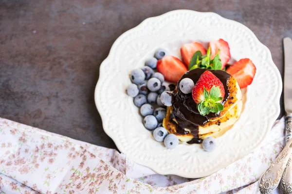 Pancakes with melted chocolate, strawberries and blueberries on a white plate