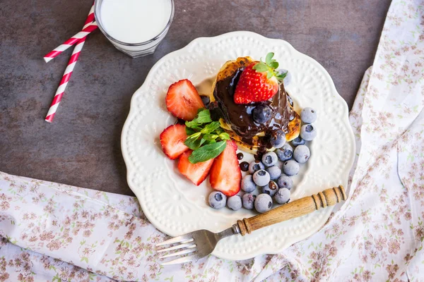 Çilek, çilek ve fincan süt ve payet ile beyaz bir plaka üzerinde yaban mersini ile Pancakes