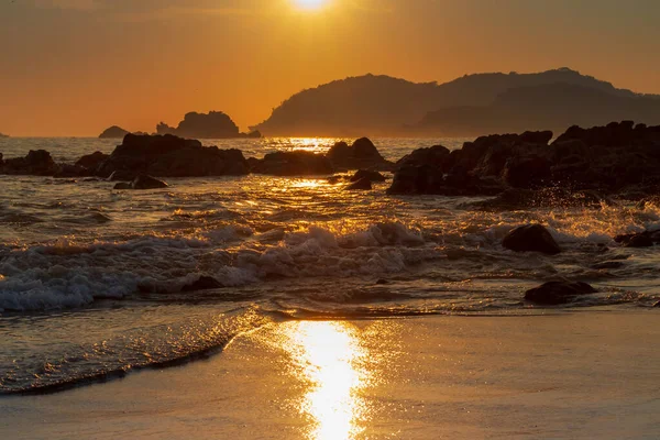 Gün batımında dağlarla çevrili deniz dalgaları