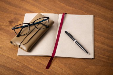 Geri dönüşümlü bitkisel malzemelerden oluşan bir defter, gözlük ve tahta masa üzerinde bir kalem.