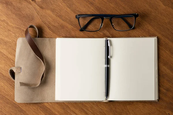 木製の机の上にレトロな革で覆われた白紙のノートと眼鏡 — ストック写真