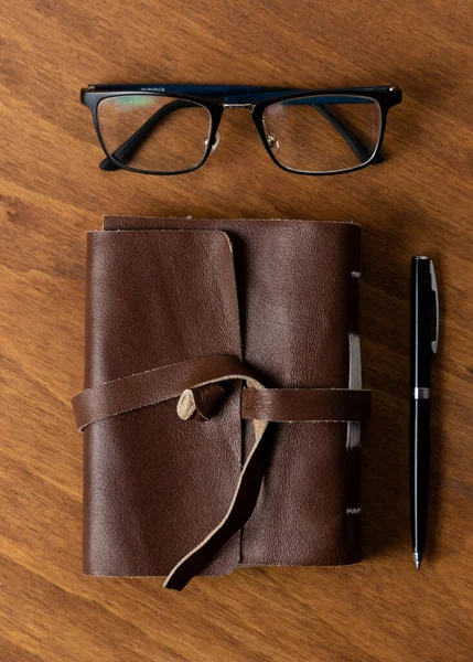 retro leather-covered blank sheet notebook and eyeglasses on a wooden desk