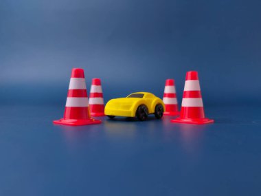 Bu resim mavi arka planda dört minyatür trafik konisiyle çevrili küçük sarı bir oyuncak arabayı gösteriyor..