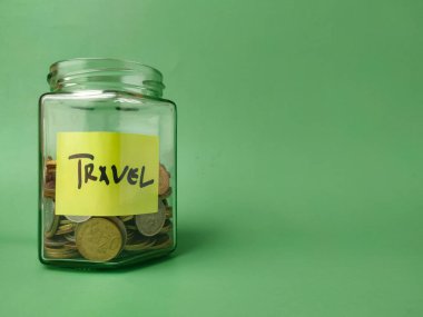 Görüntü cam bir kavanozu gösteriyor. Etiketinde TRAVEL 'in bozuk para dolu olduğu yazıyor..