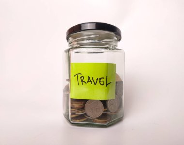 Görüntü cam bir kavanozu gösteriyor. Etiketinde TRAVEL 'in bozuk para dolu olduğu yazıyor..