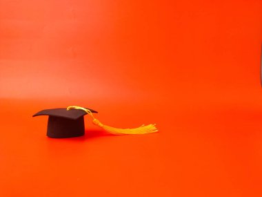 Resim, akademik başlık veya turuncu arka planda kare akademik başlık olarak da bilinen mezuniyet şapkasını gösteriyor.